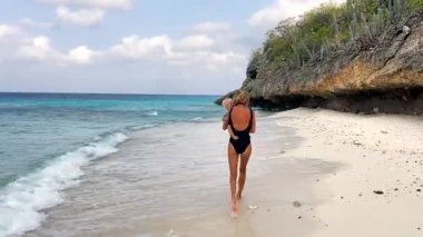 Küçük çocuğuyla el ele tutuşup güzel Karayip plajında kameradan kaçan sıska bir anne. Annem küçük bebekle gezintiye çıkmaktan hoşlanıyor.