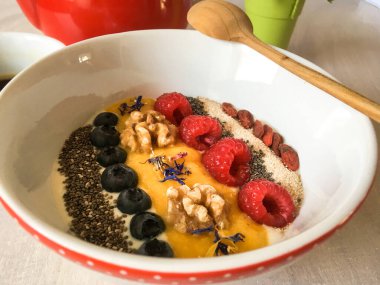 Renkli meyve, tohum ve ahşap kaşıkla süslenmiş sağlıklı kahvaltı kasesini kapatın. Yunan yoğurdu, chia, yaban mersini, ceviz, mango püresi, ahududu, susam...