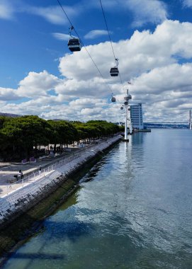 Bir teleferik yemyeşil bir parkın ve Lizbon 'daki Tejo Nehri' nin üzerinde süzülüyor. Şehir doğası ve deniz manzarasının manzaralı bir karışımı.. 