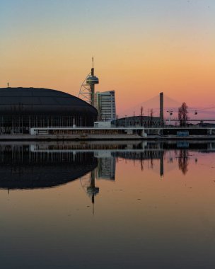 Lisbon, sakin nehri yansıtan şehir silüeti gökyüzünü canlı, renkli bir günbatımı kaplıyor. Şehir mimarisi ve doğal güzelliğin mükemmel bir karışımı..
