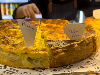 Yerel bir markette, biber ve peynir dolu canlı tabakaların sergilendiği doyurucu bir dilim hamur işi sunuluyor. Yakınlarda, renkli içecekler raflarda..