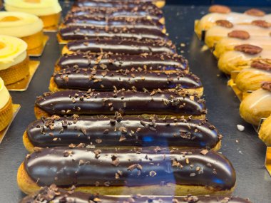 Lezzetli çikolata ekmekleri bir fırın vitrininde güzelce oturur, parlak çikolata jöleleri ve çıtır çıtır malzemeleriyle birlikte parlak ışık altında diğer tatlı ikramların yanında sergilenir..