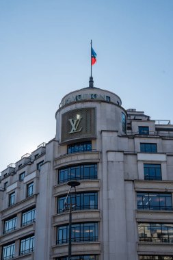 Paris. 02.02.2025. Büyüleyici bir mimari harikası güneşli bir öğleden sonra açık mavi gökyüzünde dalgalanan bir bayrak ile birlikte lüks bir butik sergiliyor..