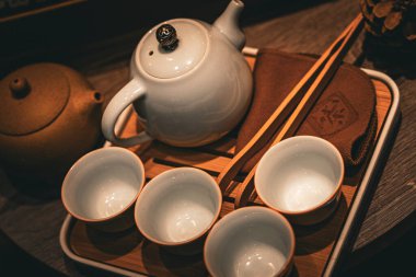 Huzurlu bir çay seti beyaz bir çaydanlık, dört narin bardak ve bambu çubukları içerir, hepsi de ahşap bir tepside zarif bir şekilde yerleştirilmiştir. Bu sahne çay içmek için ideal bir ortam yaratıyor..