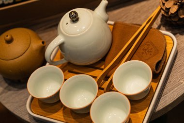 Geleneksel çay seremonisinde beyaz bir çaydanlık, dört eşleşen bardak, ahşap çubuklar ve bir çay tepsisi yer alır. Düzenleme çay kültürünün zarafetini vurguluyor..