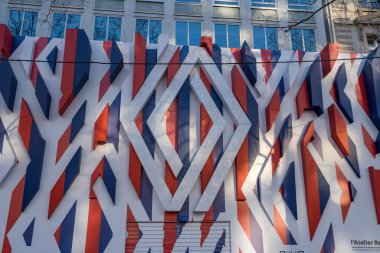 Paris. 02.02.2025. Kırmızı, beyaz ve mavi renkte çarpıcı geometrik şekillere sahip çarpıcı bir duvar resmi güneşli bir günde kentsel manzarayı canlandırır..