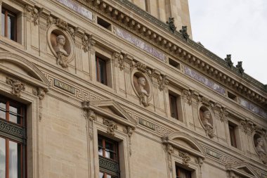 Paris, Fransa-2024-11-20 Heykelleri, bulutlu bir gökyüzü altında ayrıntılı figürler ve klasik tasarım unsurları barındıran tarihi bir binanın ön yüzünü süslemektedir. Sanatçılık kültürel mirası yansıtıyor ve