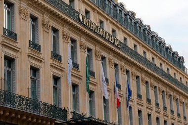 Paris, Fransa-2024-11-20 Büyük Yapı, yukarıda dalgalanan birden fazla bayrakla süslenmiş zengin bir cephe içeren karmaşık bir mimari sergiliyor. Atmosfer kentsel aktivitelerle dolu..