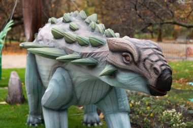 Paris, Fransa-19.2024 Büyük bir ahşap dinozor heykeli bir parkta duruyor, doğayla sanatın harmanlanmasını sağlıyor. Yaprakları sarmak huzurlu ortamı güçlendirir, ziyaretçileri davet eder