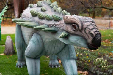 Paris, Fransa-19.2024 Dinozora benzeyen büyük bir ahşap heykel renkli sonbahar yapraklarıyla çevrili bir parkta çimlerin üzerinde duruyor. Ziyaretçiler karmaşık tasarıma ve detaylara hayran.