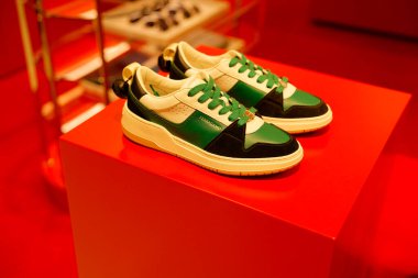 Paris, Fransa-2024-11-20 Eşsiz yeşil ve siyah aksanlı krem ayakkabılar çağdaş bir perakende alanında çarpıcı bir kırmızı ekranda sergilenmektedir. Şık tasarım dikkat çekiyor..