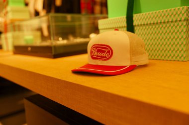 Paris, Fransa-2024-11-20 Bir perakende mağazasının ahşap rafında kırmızı ve beyaz bir şapka duruyor. Arkaplanda yeşil kutular ve mücevherlerle dolu vitrinler yer alıyor ve canlı bir alışveriş ortamı yaratıyor.