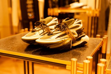 Paris, Fransa-2024-11-20 Bir çift şık spor ayakkabı modern bir perakende mağazasında parlak bir siyah masa üzerinde sergileniyor, zarif bir dekor ve sıcak ışık davetkar bir atmosfer yaratıyor.