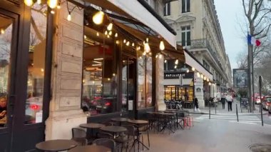 Paris, Fransa-11.01.2025 Paris caddesinde gezinirken, hareketli kafe ışıkları kaldırımı aydınlatırken müşteriler, yumuşak sohbetler ve sıcak titreşimlerle rahatlatıcı bir akşam atmosferinin keyfini çıkarıyorlar..