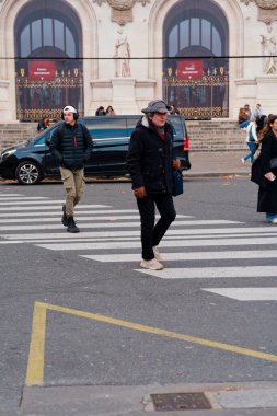 Paris, Fransa-2024-11-20 İki kişi, serin bir sonbahar öğleden sonrasında düşen yapraklarla kentsel aktivitelerle çevrili tarihi bir yapının yakınındaki yaya geçidinde geziniyor..