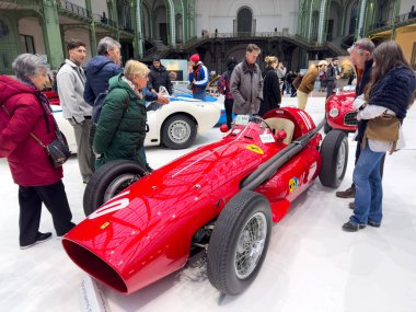 Paris, Fransa-04.02.2025 Ziyaretçiler, büyük bir salonda gerçekleşen hareketli otomotiv gösterisi sırasında dizaynı ve tarihiyle büyülenen klasik bir Ferrari 'nin etrafında toplandılar..