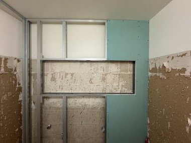 Drywall installation progresses in a room, featuring unfinished walls and metal framing. Workers prepare to cover the bare drywall with new material. clipart