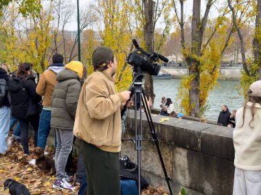 Seine Nehri kıyısındaki bir toplantıda halk arasında eğlenen bireyler yer alıyor. Bir film yapımcısı, düşmekte olan yapraklar ve sonbahar renkleri arasında kamerayla anı yakalar..