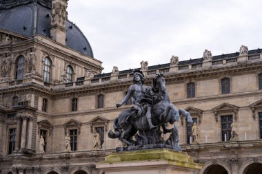 Çarpıcı bir heykel, Paris 'teki ikonik Louvre Müzesi' nin önünde at süren bir savaşçıyı resmediyor. Tarihi yapılar mimari ve heykelleri karmaşık bir şekilde sergiliyor..