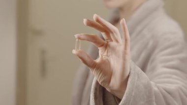 Güne hazırlanırken bornozlu bir kişi bir Omega 3 kapsülü tutuyor. Parlak, rahat bir yerde. Bu, Omega 3 'ün günlük sağlık uygulamalarına dahil edilmesinin önemini vurgular..