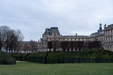Ziyaretçiler Paris 'teki tarihi binalarla çevrili iyi korunmuş bir bahçede geziniyorlar. Hava sakin, bulutlu gökyüzü kışın yaklaştığını gösteriyor..