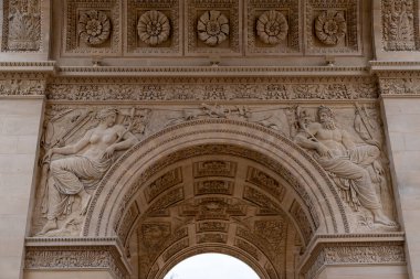 Süslü oymalar klasik figürleri bir Avrupa şehrindeki anıtsal bir yapının kemerinde tasvir ederek, tarihi sanatçılık ve zanaatkarlık sergiliyor. Detaylar zarafeti vurgular.