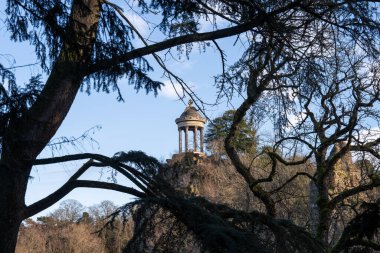 Ziyaretçiler, Parc des Buttes-Chaumont 'un dingin güzelliğinin tadını çıkarıyorlar. Sibylle Tapınağı' nın görkemli bir şekilde mavi gökyüzüne karşı durduğu, yemyeşil ağaçların çerçevelediği yerde..