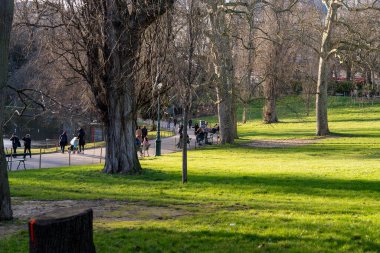 İnsanlar Parc des Buttes-Chaumont 'ta dolambaçlı yollarda yürürken güneş ışığı ağaçların arasından akar. Yeşillik ve sakin atmosfer rahatlamak için mükemmel bir ortam yaratır..