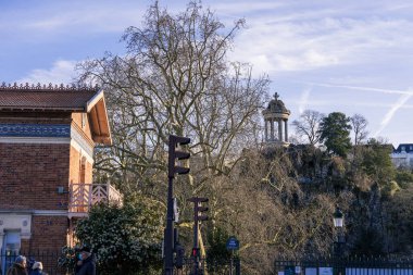 Ziyaretçiler bir kış öğleden sonra Parc des Buttes-Chaumont 'ta dolaşarak huzurlu atmosferin, tarihi yapıların ve bölgeyi çevreleyen doğal güzelliğin tadını çıkarıyorlar..