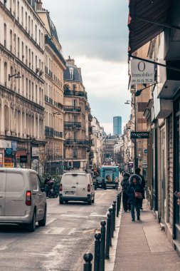 Paris 'teki hareketli bir cadde, her iki tarafında büyüleyici binalar bulunan mimari tarzların bir karışımını gözler önüne seriyor. Yayalar kaldırım boyunca yürürken araçlar otoyolda ilerler. Atmosfer