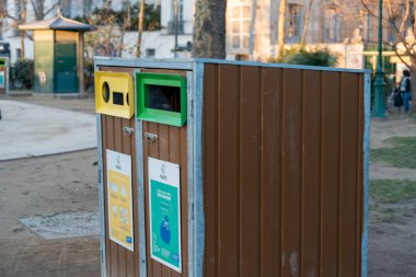 Paris, Fransa-13.01.2025 kalabalık bir halk parkında, çöp ve geri dönüşümlü malzemeler için tasarlanmış iki ayrı çöp kutusu yan yana duruyor. Kahverengi çöp tenekesi genel atık içindir.