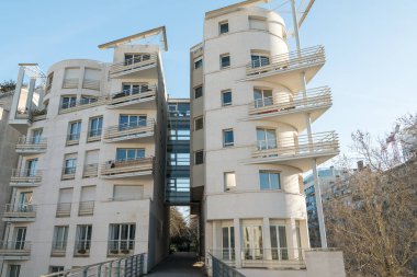 Paris, Fransa-14.01.2025 Benzersiz çok katlı bir binada, gün ışığında yeşil ve diğer yapılarla çevrili kıvrımlı balkon ve geniş pencereli modern mimari sergileniyor..