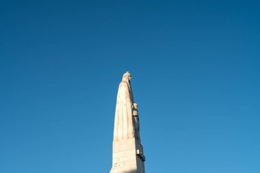 Uzun, etkileyici bir taş heykel, açık mavi gökyüzüne karşı yükselir ve tarihi önemin özünü yakalar. Eserde karmaşık ayrıntılar yer alıyor, sanatsal zanaatkarlık sergileniyor.