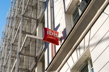 13 Ocak 2025 'te Paris, Fransa' da canlı bir Ibis oteli mavi gökyüzüne karşı durmaktadır. Bina, temiz çizgiler ve geniş pencerelere sahip çağdaş mimari tasarım sergiliyor.
