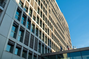 Paris, Fransa-14.01.2025. Uzun, modern bir şehir binası, açık mavi gökyüzüne karşı eşsiz mimari tasarımını sergiliyor. Yapıda geniş pencereler ve farklı çizgiler yer alıyor.