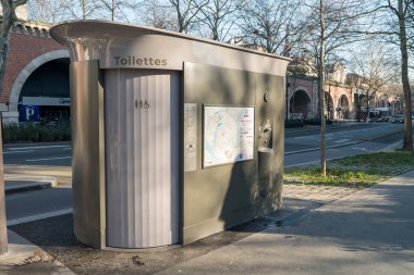 Paris, Fransa-14.01.2025 Şık bir umumi tuvalet yapısı kalabalık bir caddenin yanında duruyor ve ziyaretçilere konfor sunuyor. Yakınındaki ağaçlar gölge oluşturarak kentsel manzarayı güçlendirir..