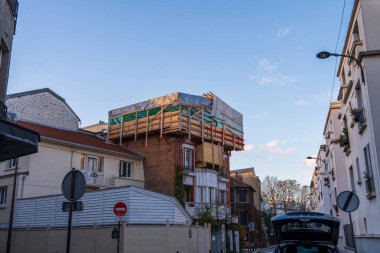 İnşaat işçileri kalabalık bir kentsel mahalledeki çok katlı bir binayı aktif olarak yeniliyorlar. Yapı belirgin bir şekilde iskelelerle destekleniyor ve koruyucu malzemelerle kaplanıyor