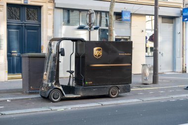 Paris, Fransa-14.01.2025. Küçük bir teslimat aracı, arka planda dükkanlar ve binalar bulunan kalabalık bir cadde boyunca park halinde. Gökyüzü açık, parlak bir gündüz ayarını gösteriyor..