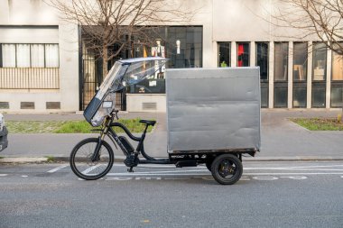 Paris, Fransa-14.01.2025 Bir kargo bisikleti şehir caddesinde park halinde duruyor. Aracın kargo alanı üzerinde koruyucu bir koruması var. Yakınlarda, binalar ve ağaçlar tipik bir kentsel zemin oluşturuyor.