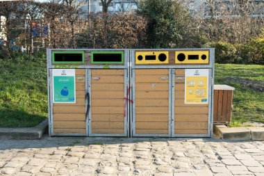 Paris, Fransa-14.01.2025 Bir geri dönüşüm istasyonu ahşap ve metalden yapılmış iki büyük kutuya sahiptir. Her kutunun yeşil bir alanda bulunan plastik, kağıt ve camı ayırmak için farklı açıklıkları var..