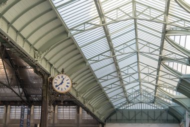 Paris,France-14.01.2025 A striking clock hangs from intricately designed ironwork, showcasing the beauty of vintage train station architecture with a soaring glass roof allowing natural light. clipart