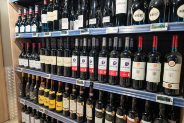 Raflarda çeşitli şarap şişeleri sergileniyor. Parisli bir mağazada canlı bir seçim. Çeşit çeşit şaraplar farklı bölgelerden, her biri farklı betimlemelerle etiketlenmiş kırmızı şaraplar ve