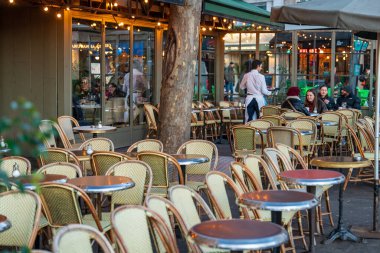 Paris, Fransa-13.01.2025 renkli açık hava koltukları kalabalık bir şehir bölgesindeki canlı bir kafede müşterileri bekliyor. Bistro tarzı masalar ve hasır sandalyeler davetkar atmosferi vurgular.