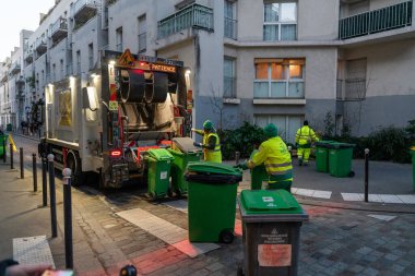 13 Ocak 2025 'te Paris' in göbeğinde kendini işine adamış bir sokak temizleme ekibi görevlerini yerine getiriyor. Parlak sarı ve yeşil üniformalı işçiler, verimli bir şekilde yeşil atık kutularının etrafında toplanıyorlar.