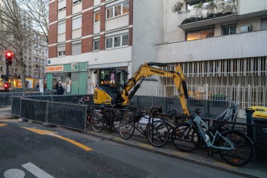 13 Ocak 2025 'te Paris, Fransa' da bir caddede inşaat çalışmaları devam ediyor. Sarı bir kazıcı bisiklet raflarına güvenle park edilmiş, kısmen engellenmiş bir bisiklet koleksiyonunun yanında duruyor.