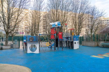 Çocuklar için tasarlanmış canlı bir oyun alanı uzun ağaçlarla çevrili bir şehir parkında duruyor. Yapıda çocukları davet eden birden fazla slayt, tırmanma alanları ve etkileşimli oyun panelleri yer alıyor.