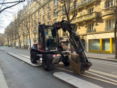 Paris, Fransa-16.02.2025 Sağlam bir inşaat aracı, zarif mimari ve çıplak ağaçlarla çevrili caddenin bir bölümünü özenle temizlemek için çalışır..