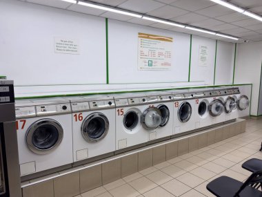 Paris, Fransa-20.02.2025 Kendi kendine hizmet eden çamaşır makinelerinin sıraları temiz bir çamaşırhanede kullanılmaya hazır, parlak ışıklarla aydınlatılmış, uygun çamaşır günleri için mükemmel.