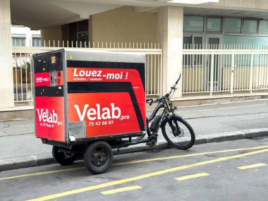Paris, Fransa-21.02.2025 Çağdaş bir binanın yakınındaki caddede canlı bir teslimat bisikleti duruyor, şehir zemininde parlak bir tasarım sergiliyor, merak ve keşifleri davet ediyor..