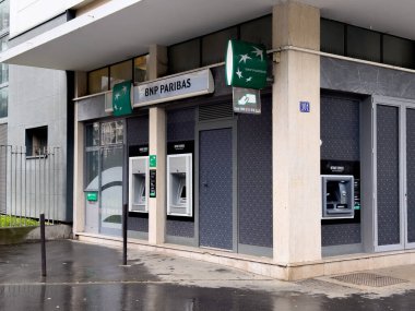 Paris, Fransa-25.02.2025 Yağmurlu sokaklar çağdaş bir bankanın zarif mimarisini yansıtıyor. Otomatik veznedar makineleri uygun para çekmek isteyen müşteriler için hazır bekliyor.